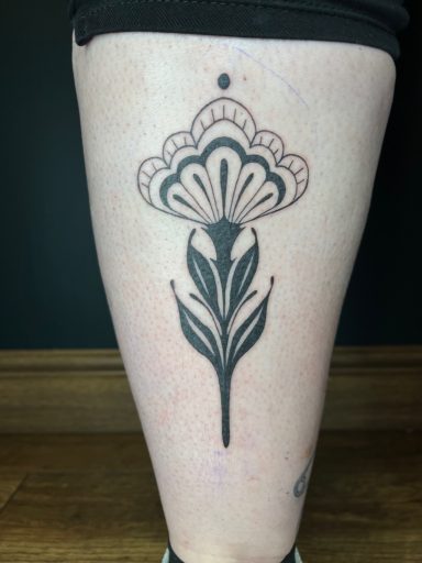 A black tattoo of a stylised flower with intricate details on a leg.