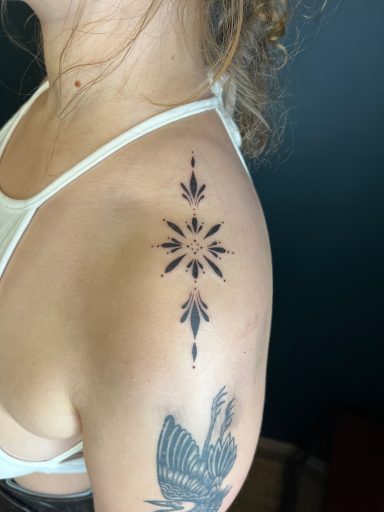 Black ink tattoo on the upper arm featuring a star-like design with floral elements.