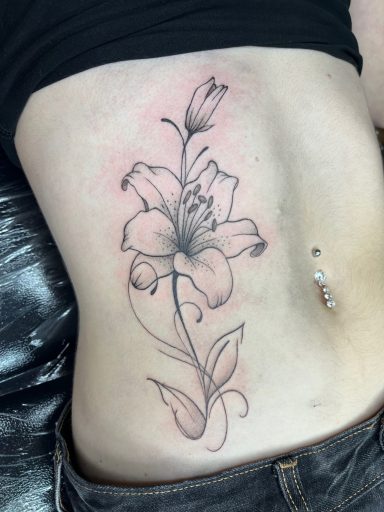 Tattoo of a lily flower on the side of a person's torso.
